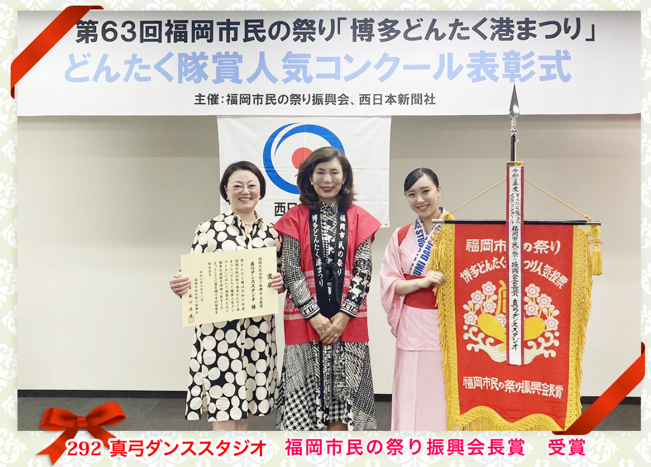 どんたく隊賞人気コンクール表彰式にて会長と真弓ダンススタジオ主宰小林真弓が賞状待ち、生徒代表が入賞旗を待ち3人並んで。
