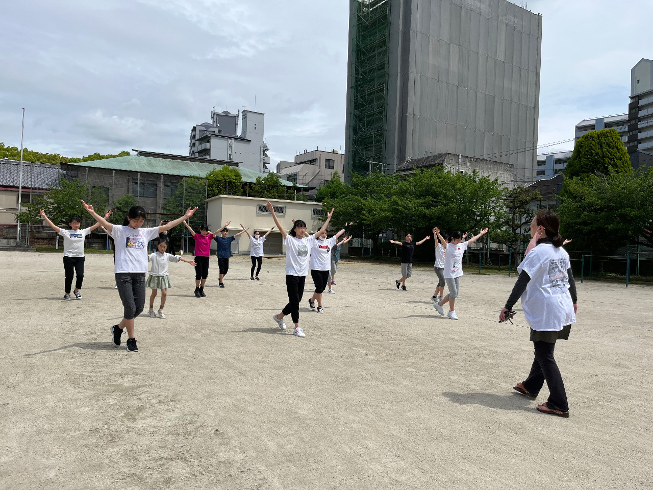 中高生の大人クラスの生徒がグラウンドで両手を挙げて踊っているところ