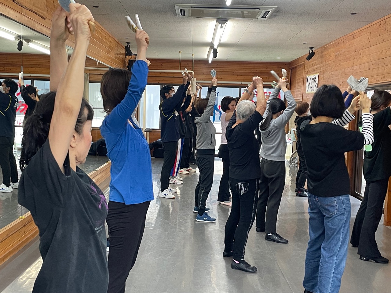20名ほどのメンバーが両手をあげてシャモジを打ちながら踊りの練習をしている写真