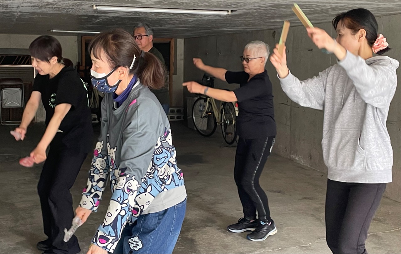 5人の男女が両手を左右に振りながら踊りの練習をしている写真