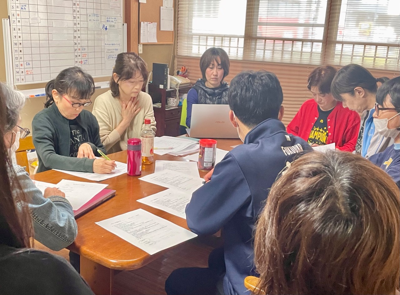 部屋に中10人近くの男女が集まって会議をしている