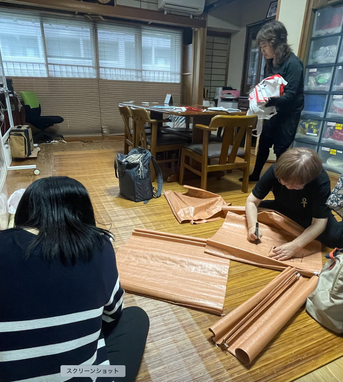 事務所の畳の上でパレード用の旗や荷物管理用の袋を準備するスタッフ