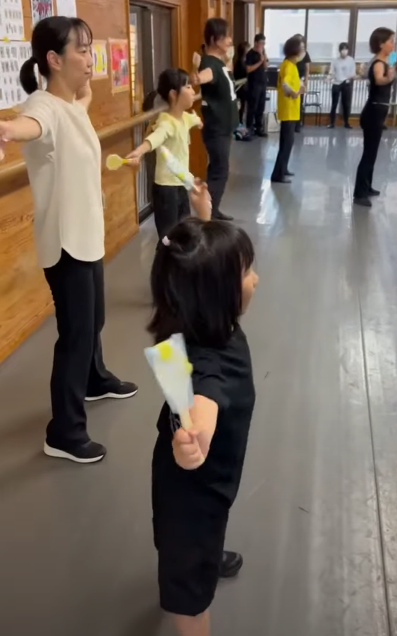 大人に混ざって両手を大きく開き踊っている女の子