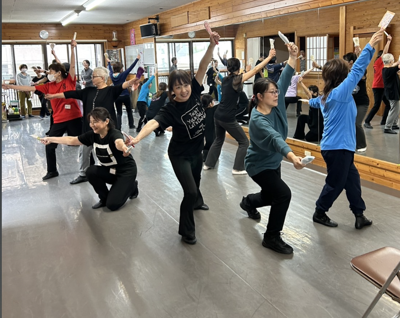 練習スタジオで10人ほどのメンバーが中央に集まり外を向いて両手を広げアピールの練習をしている