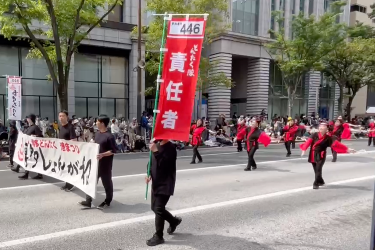 パレードの先頭のフラッグや垂れ幕の後ろを踊るしょんがね隊