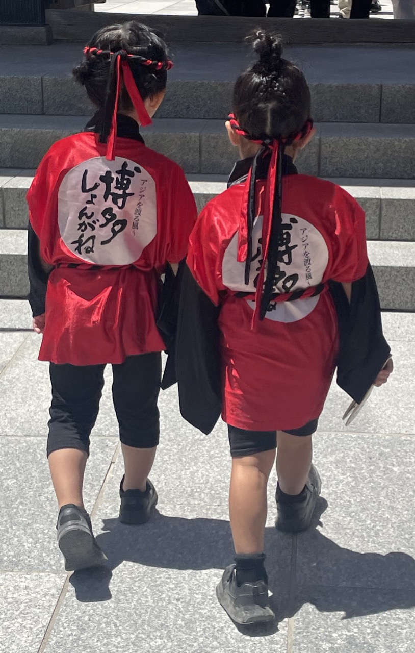 博多しょんがね隊の衣装を着た2人の女の子が手を繋いで歩く後ろ姿